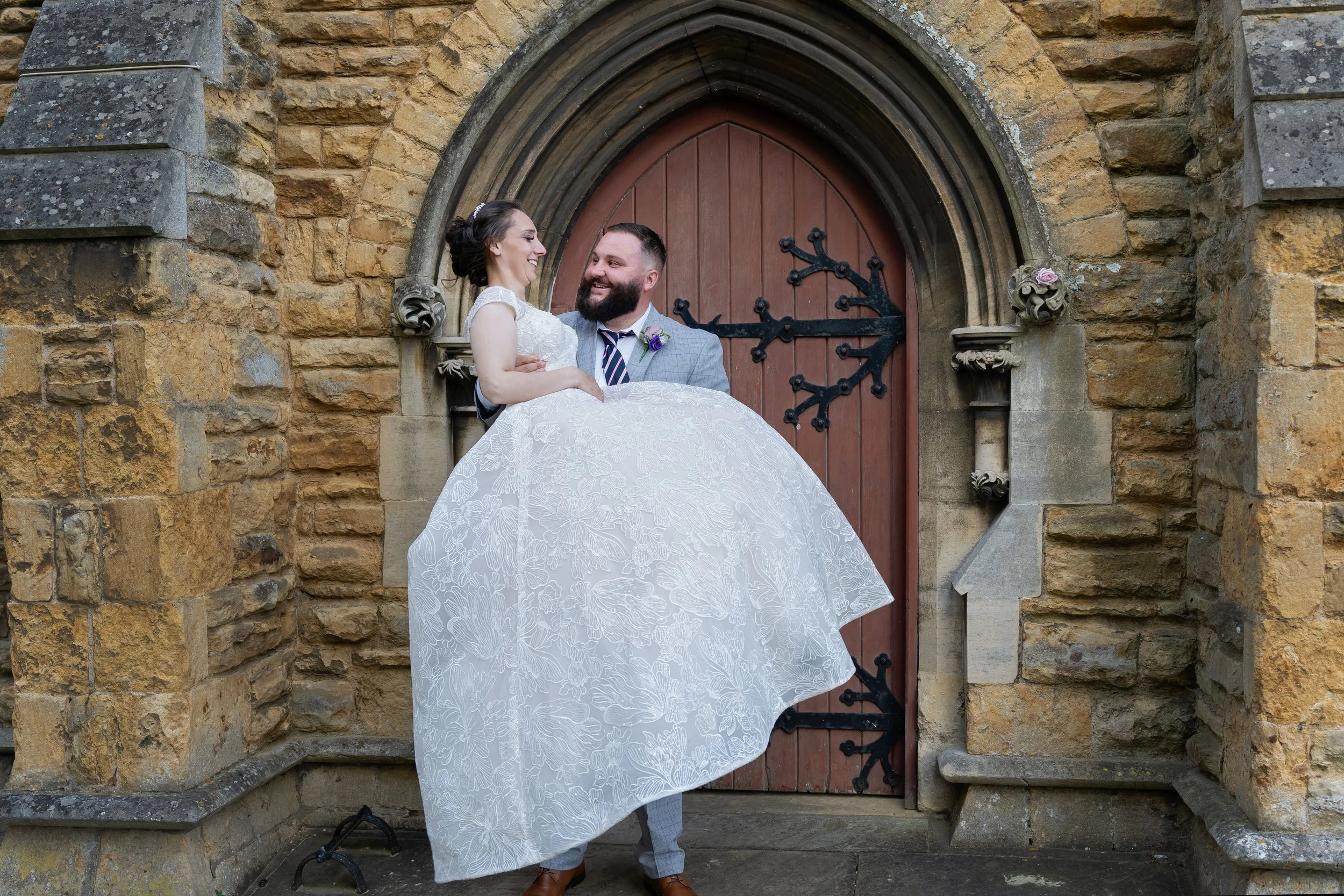 Groom picking up bride, outside church doors in North hykeham, Lincoln. They are looking at each other smiling.