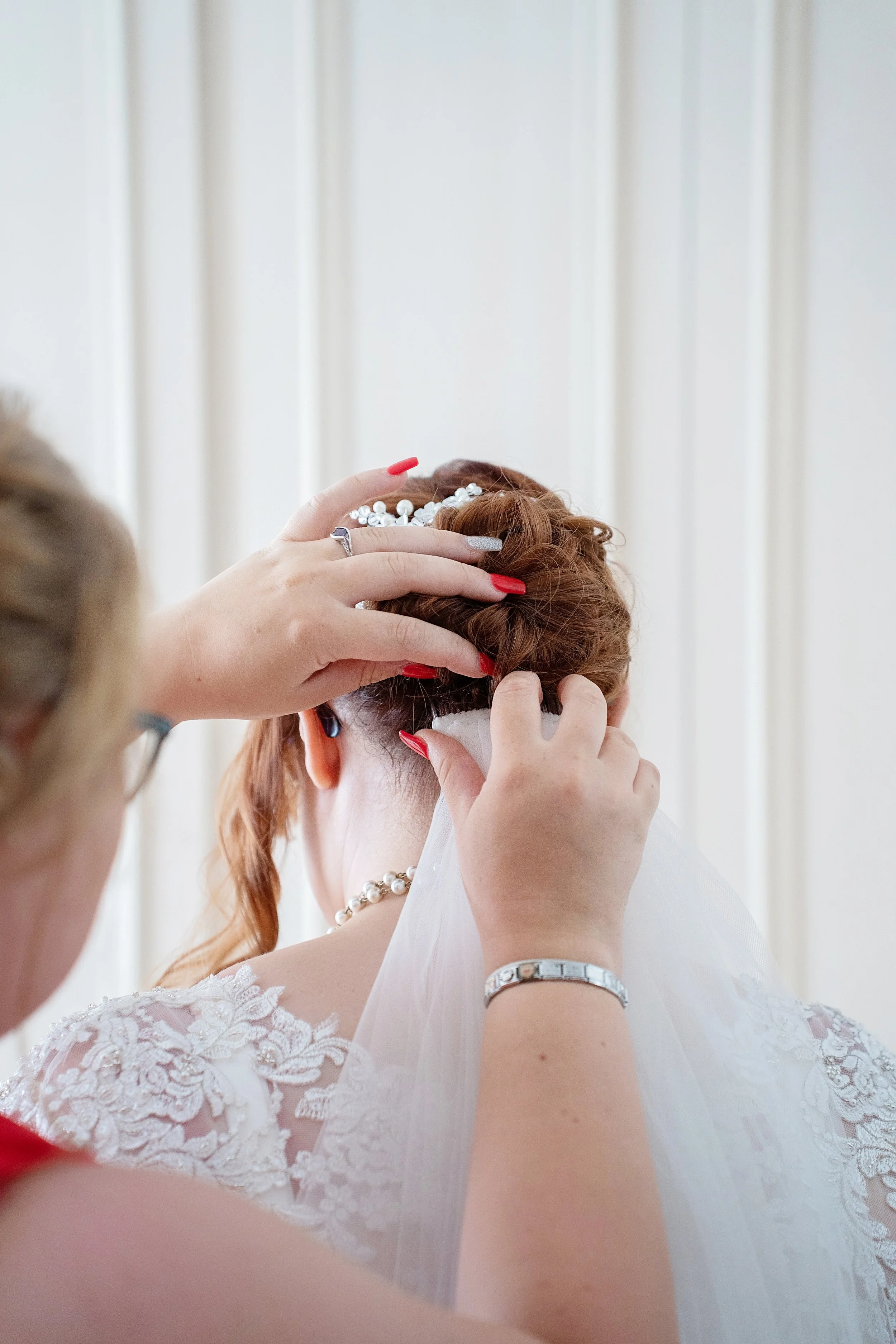 Bridesmaid putting vail in brides hair, at the back of her head - colour photo