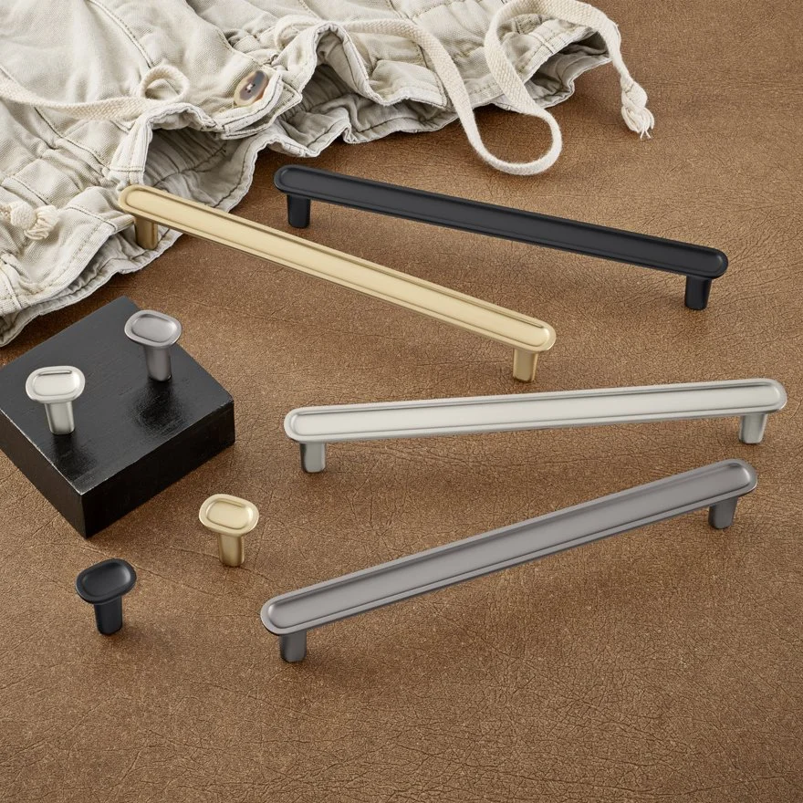 Colorful cabinet handles in black, beige, white, and gray, displayed on a brown surface with a beige pair of pants in the background.