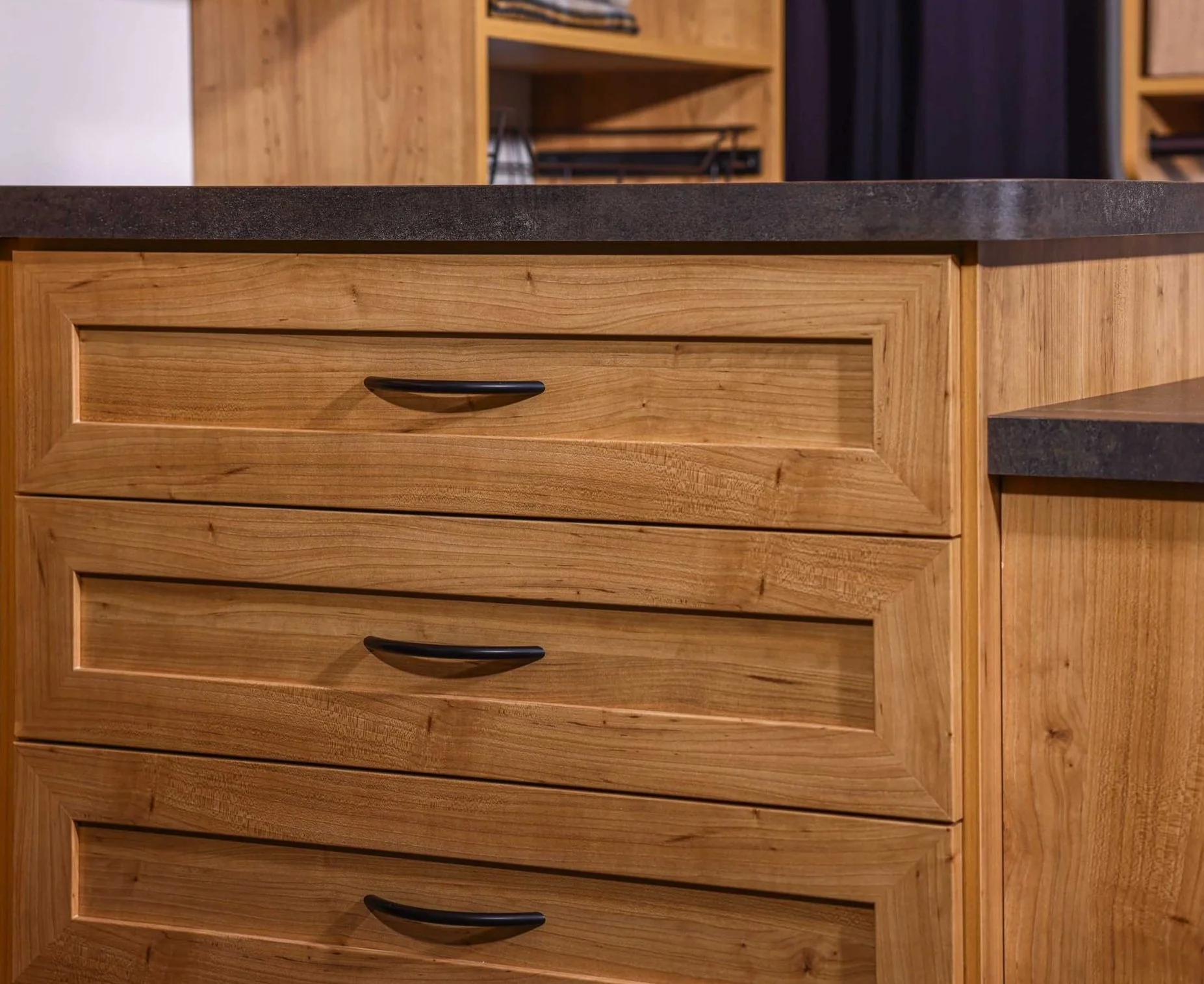 Wooden closet cabinets with black handles and dark countertop.