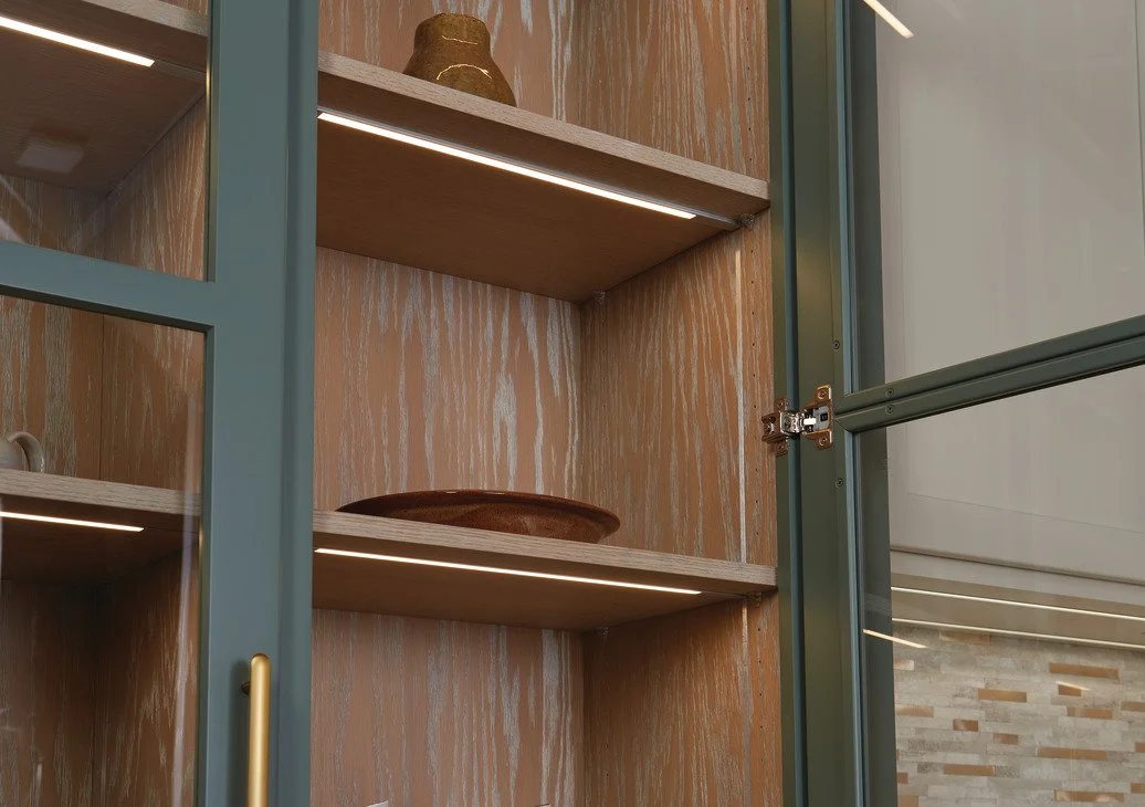 Wooden cabinet with glass door, interior shelves, decorative pottery pieces, and recessed lighting.