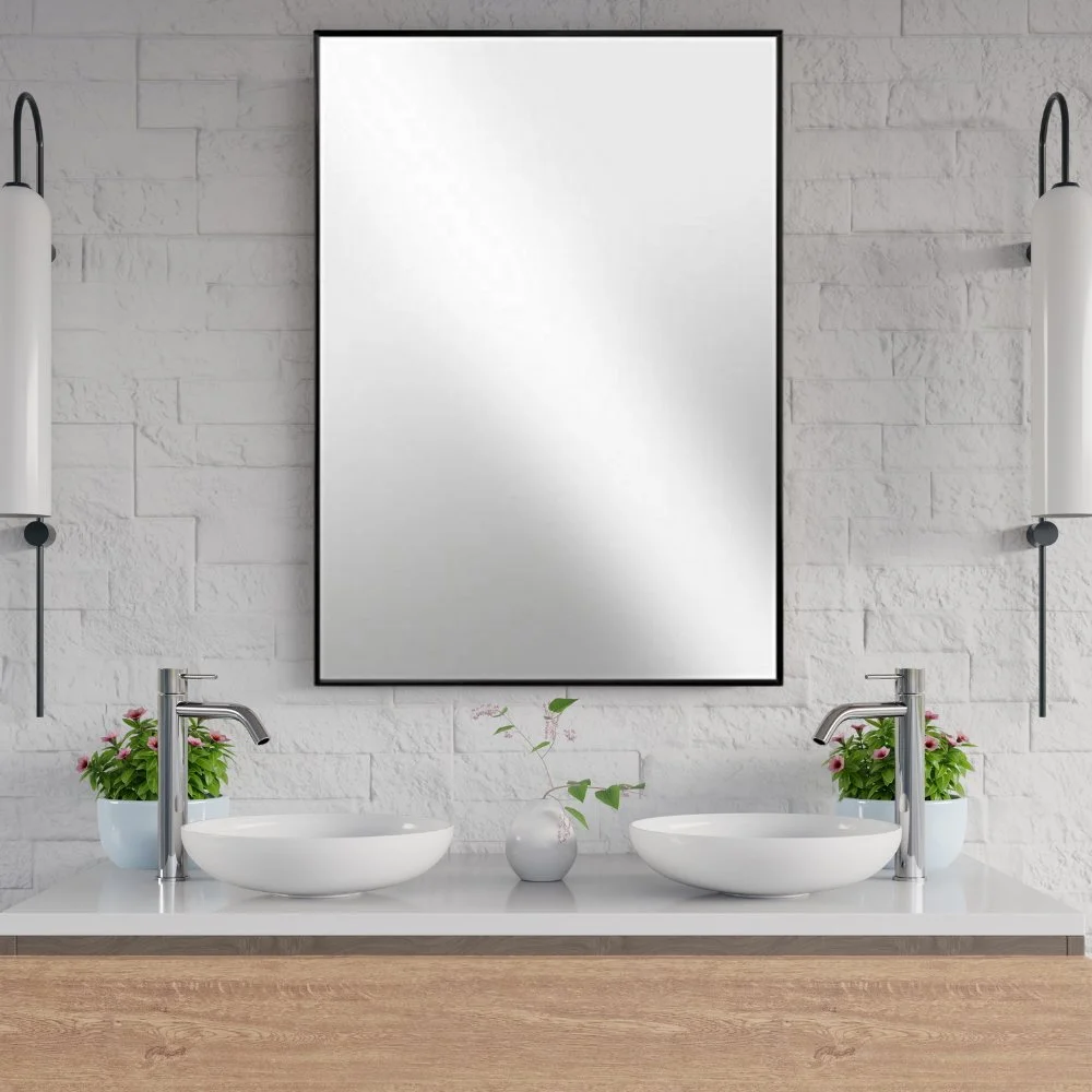 Modern bathroom vanity with double sinks, large rectangular mirror, and decorative plants on a white countertop against a textured brick wall.