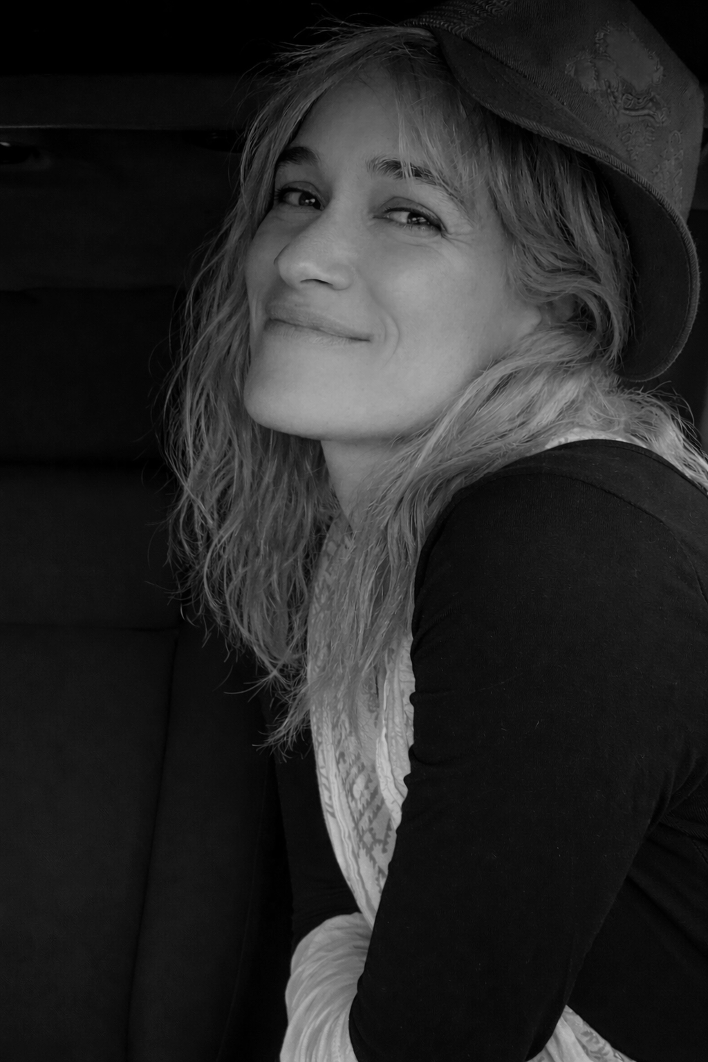 A woman with tousled brown hair wearing a navy and white polka dot sleeveless top with tied straps, standing against a plain light-colored background.