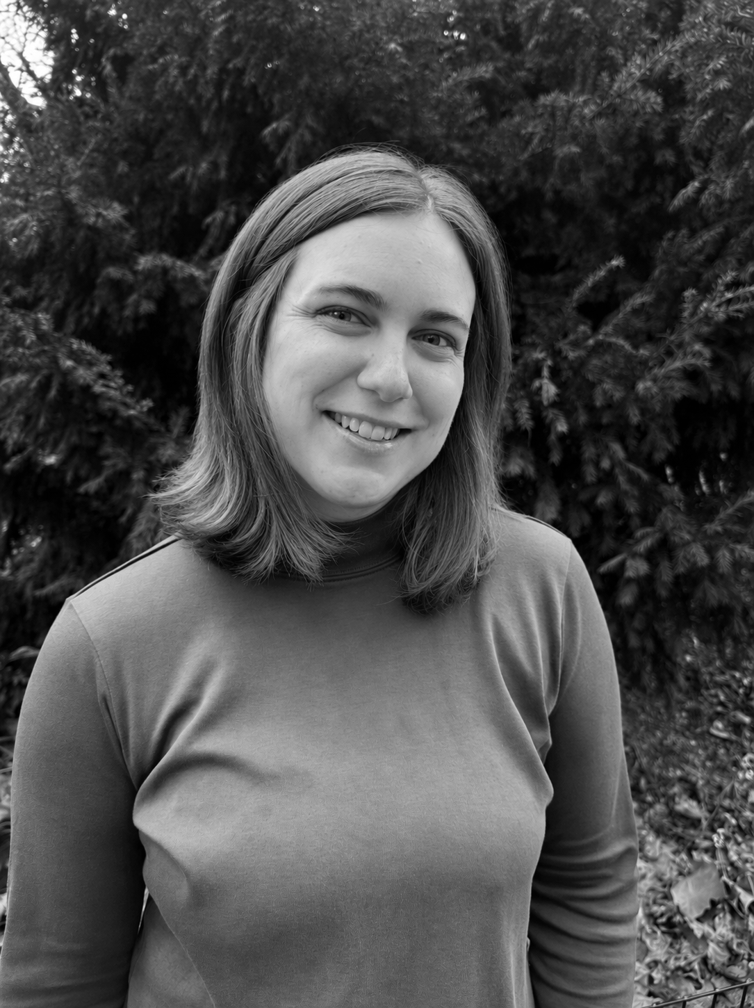 A woman smiling outdoors with trees in the background.