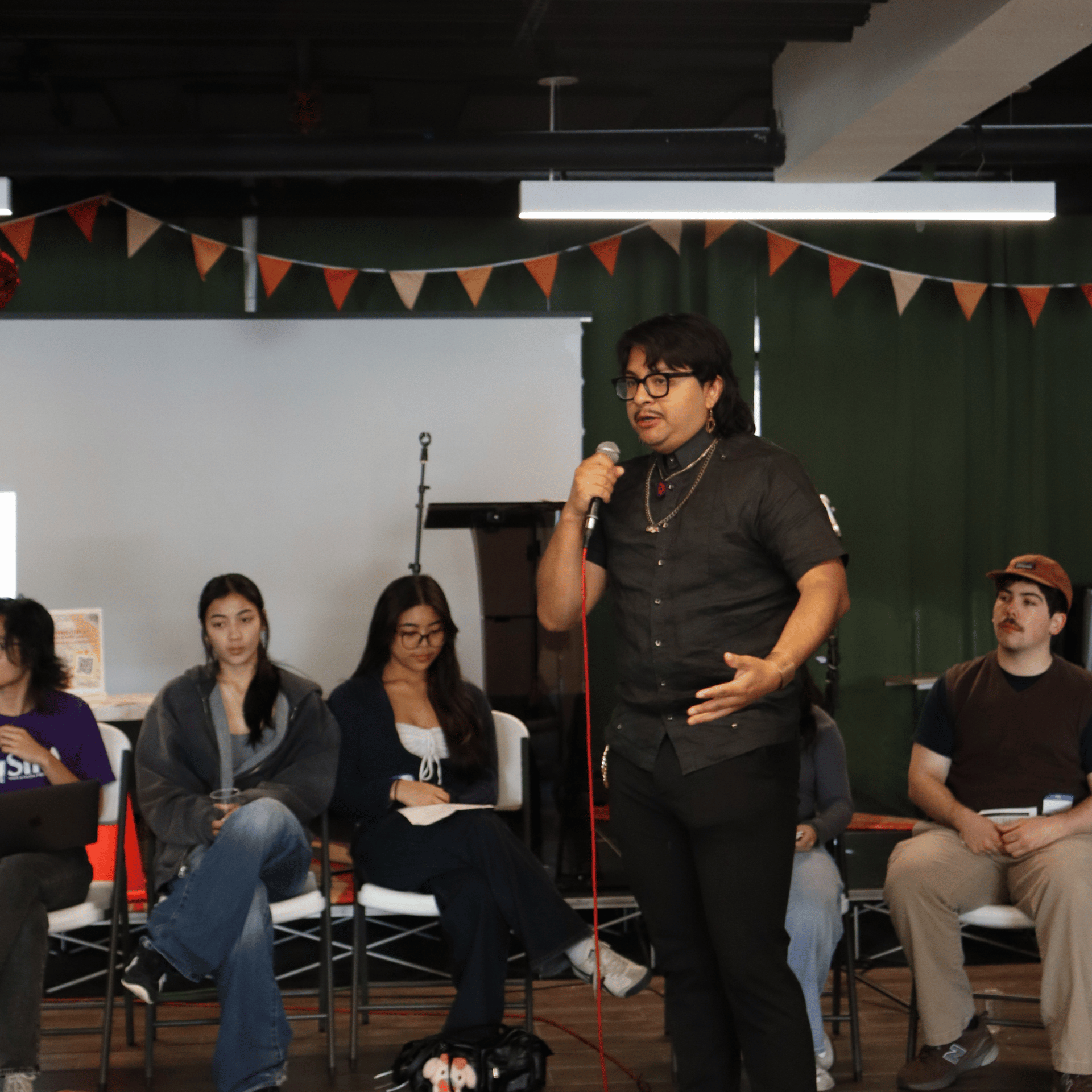 A young man with a mic stands in front of a group of seated young adults