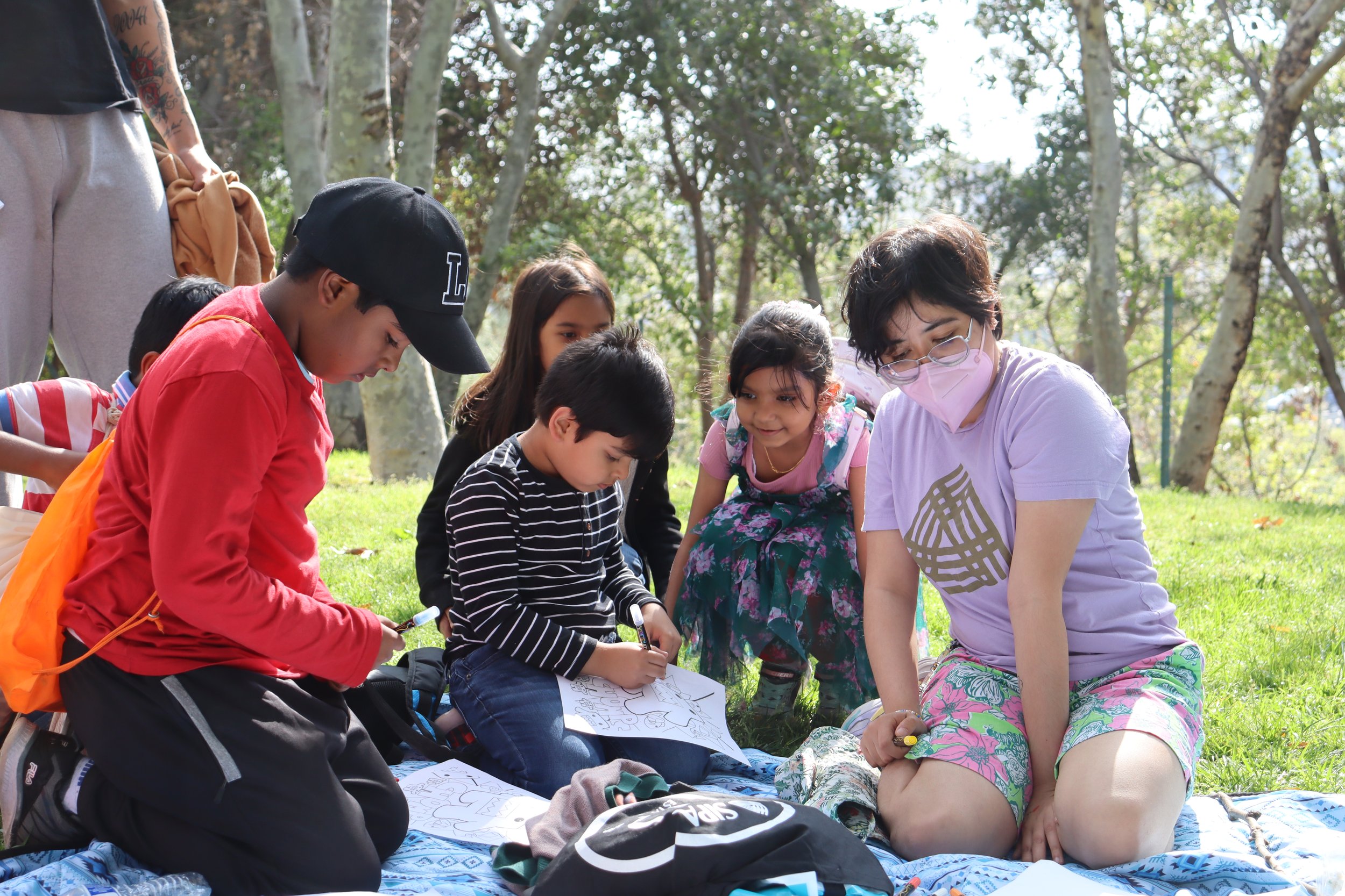 Four young kids color with a SIPA staff person in a park