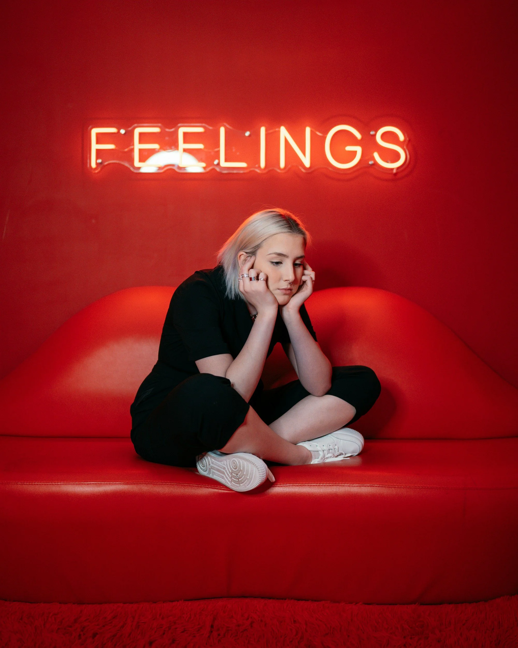 Person sat on sofa with head in hands, against a red wall with feelings illuminated behind them