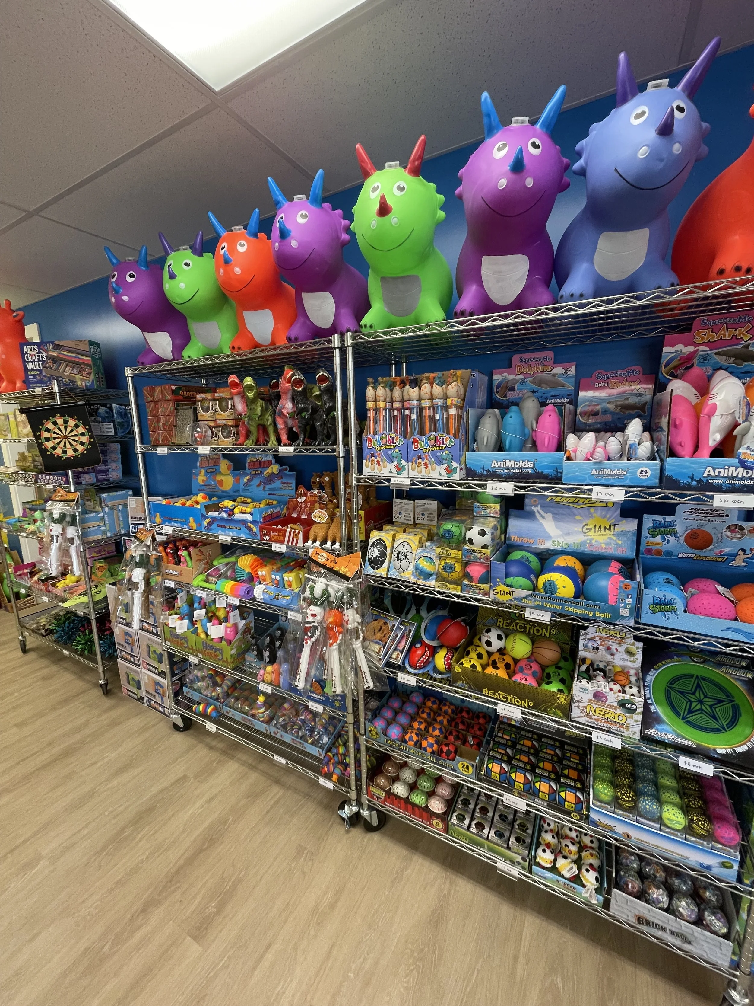 Colorful shelves display various toys including inflatable unicorns, robots, and balls in a store.