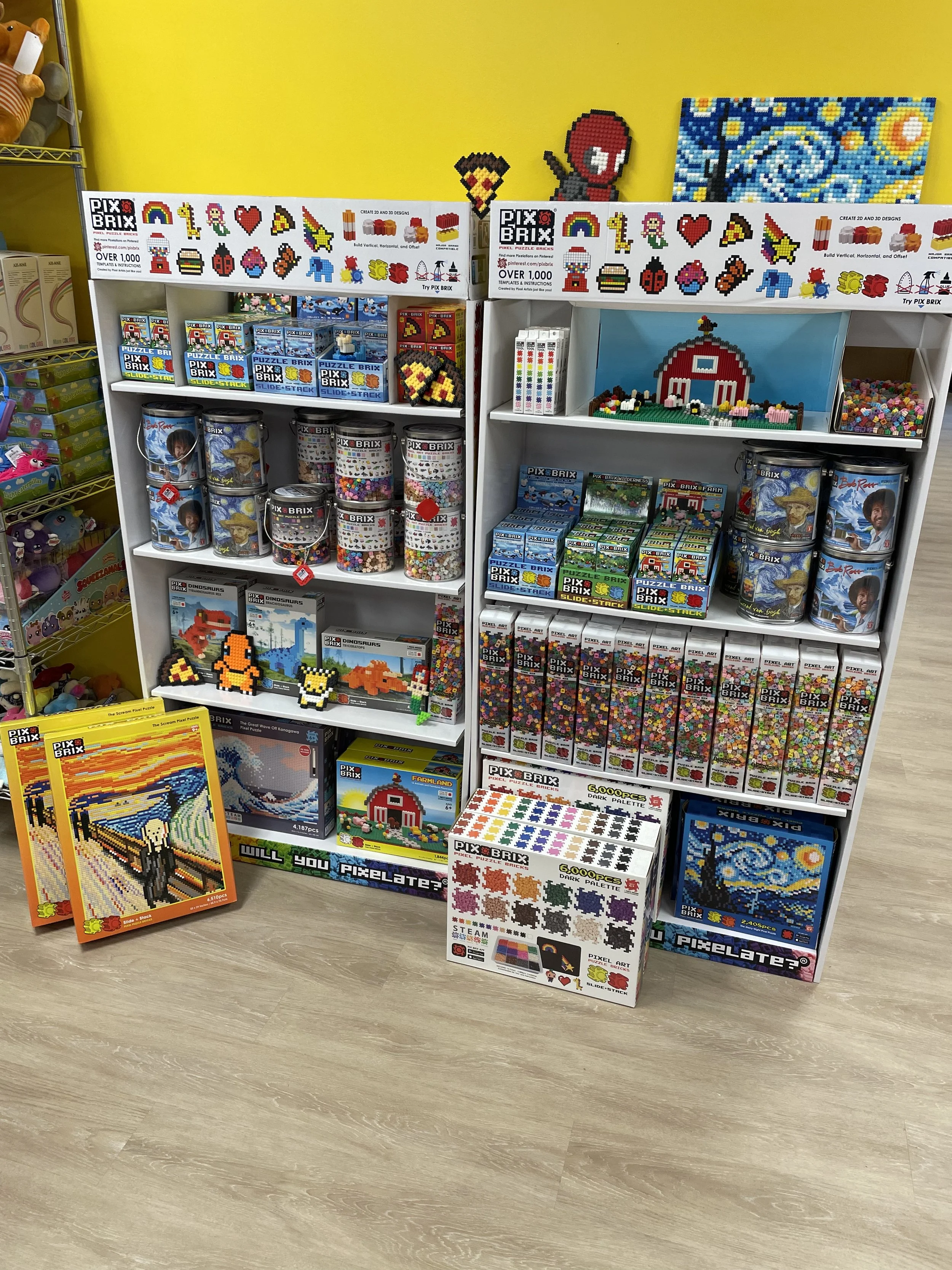 Display shelf filled with Pix Brix building kits, pixel art toys, and assembled pixel art creations against a yellow wall.