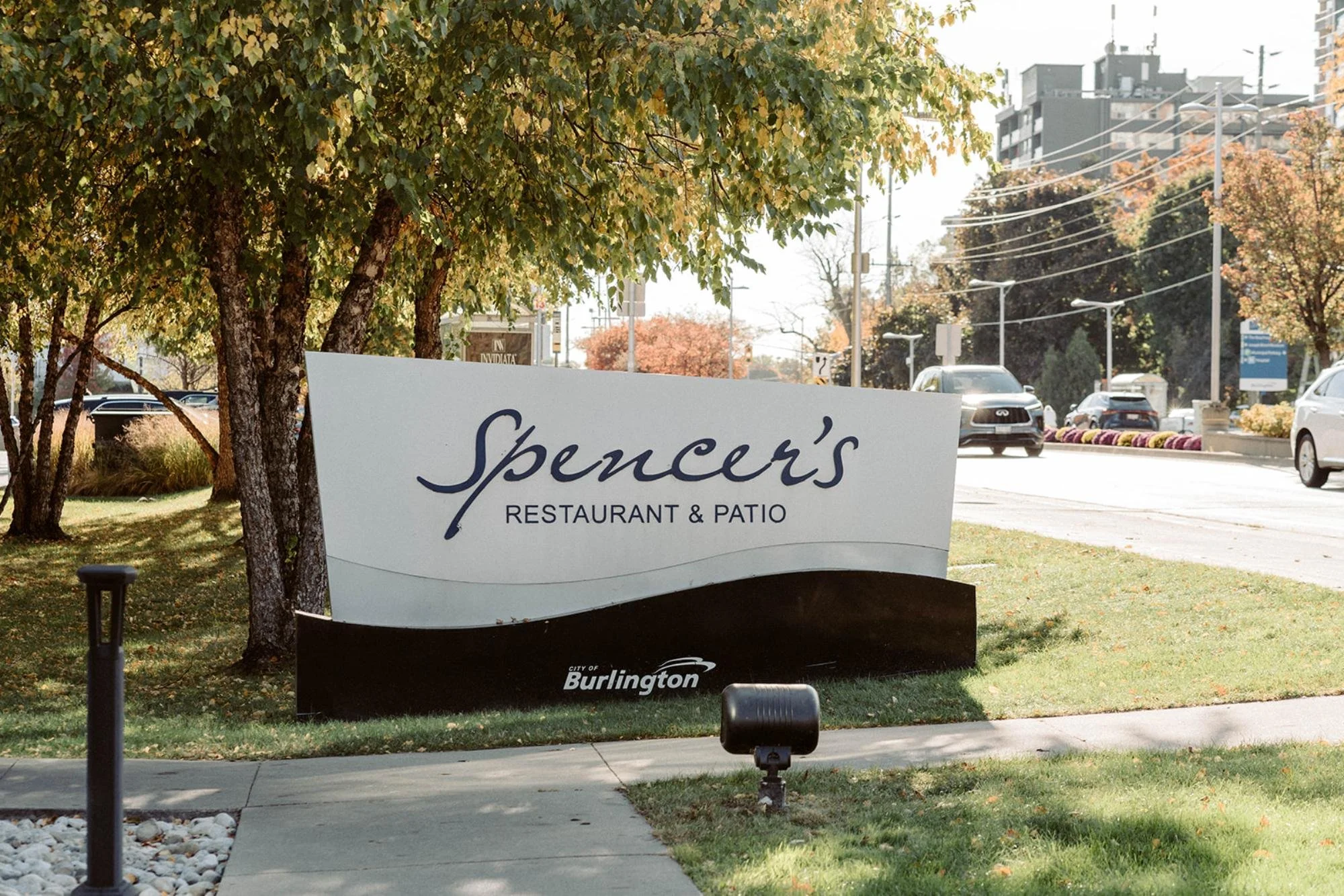 Street sign for Spencer’s Restaurant &amp; Patio surrounded by trees and passing cars.