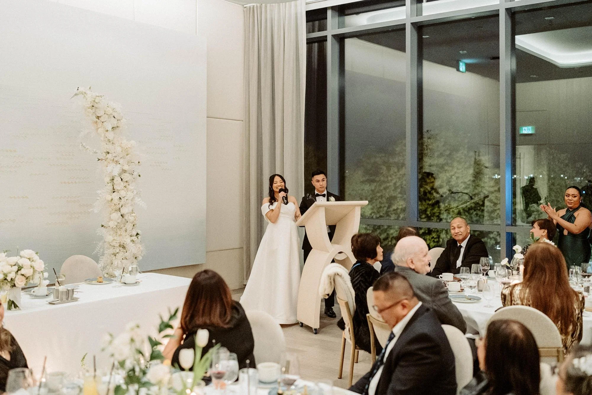 Bride and groom give a speech at the podium while guests watch during the reception.