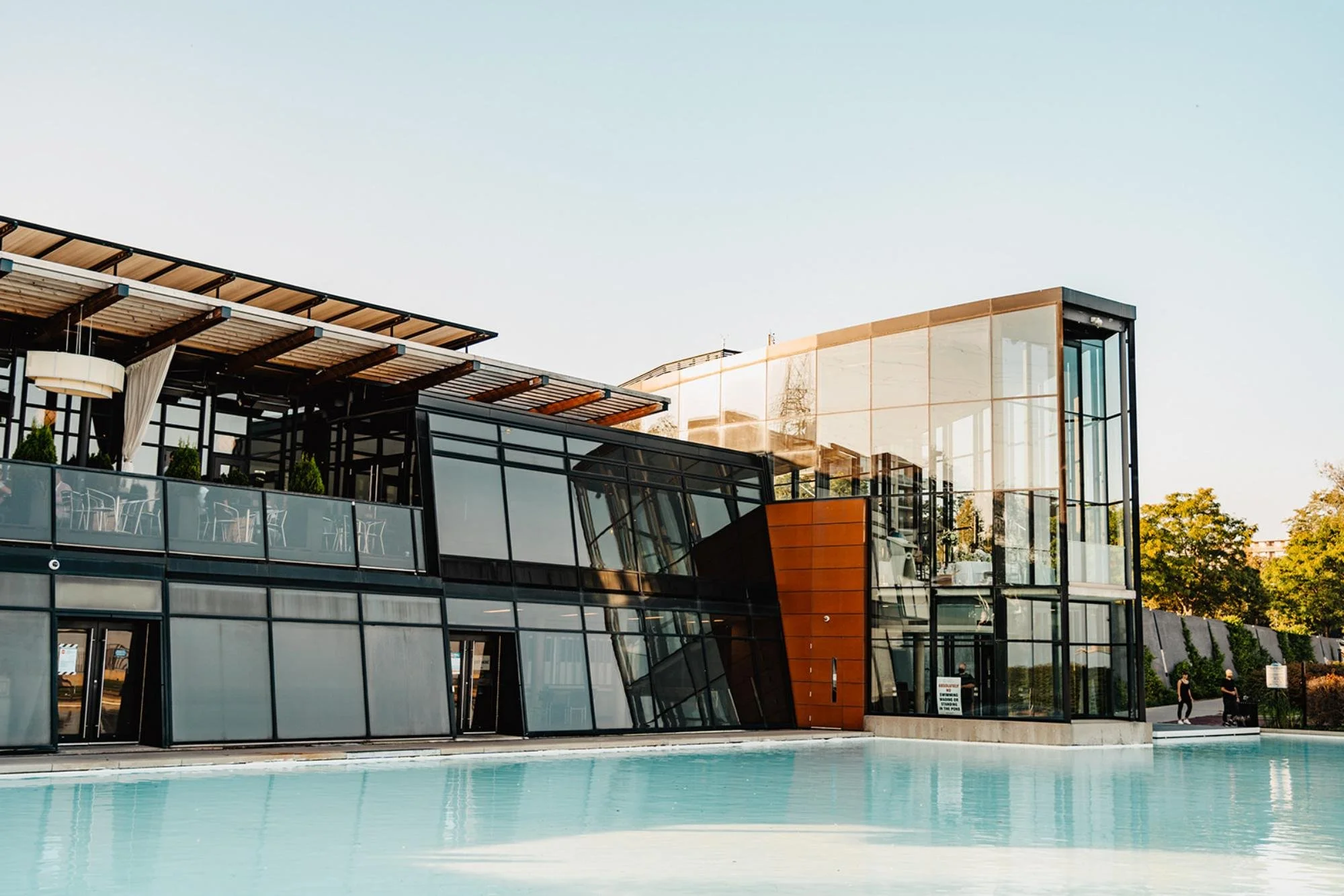 Exterior view of a modern waterfront building with large glass walls and a pool.