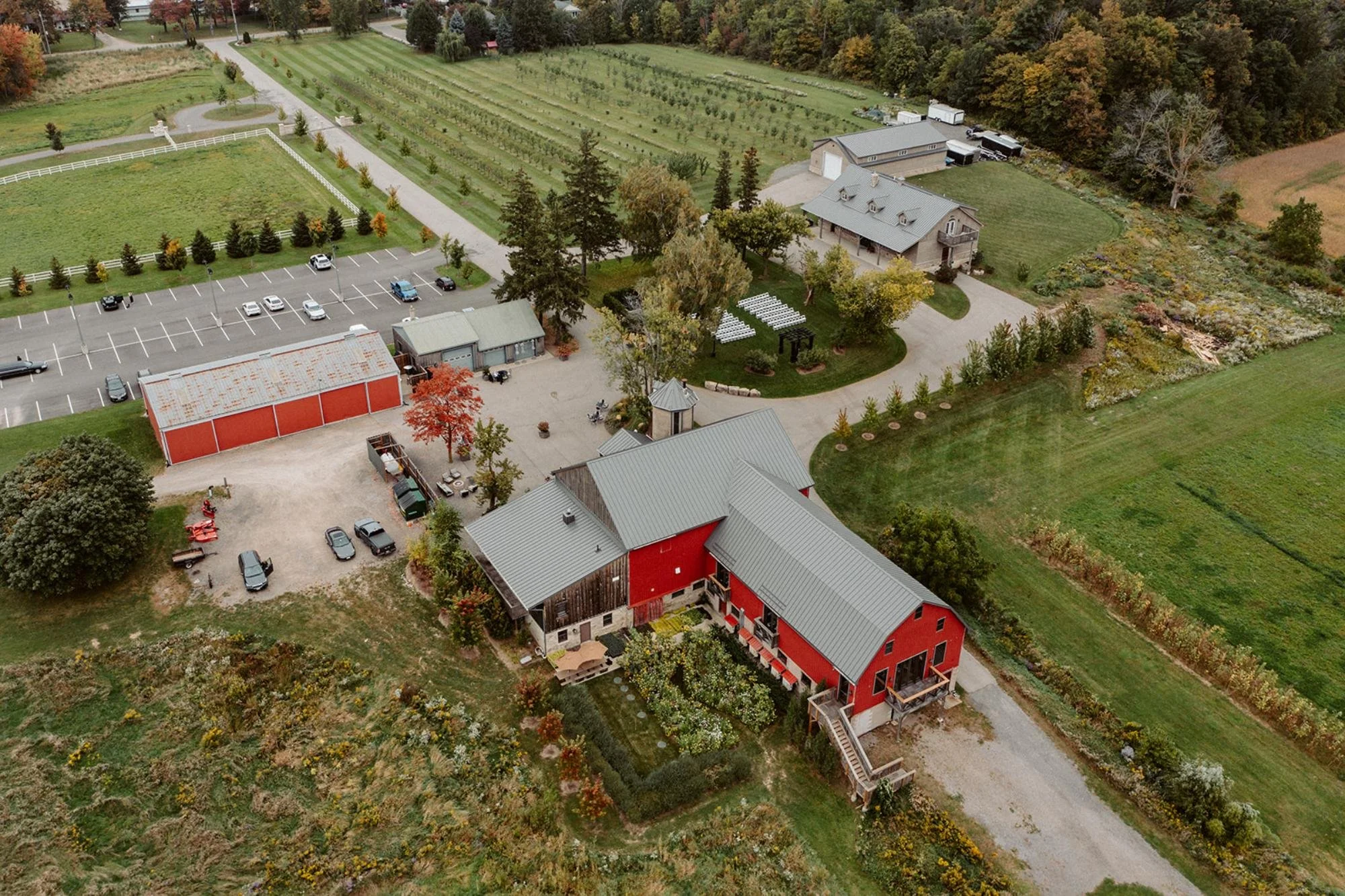 Aerial view of a red barn venue with nearby buildings, parking area, and tree-lined grounds.