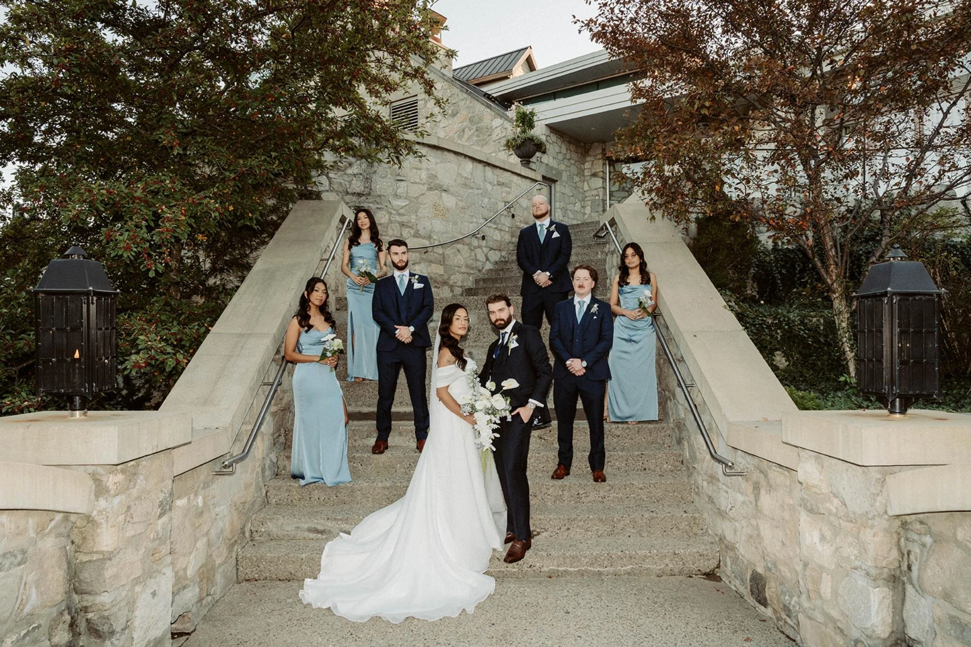 Bride and groom standing on a stone staircase with their wedding party arranged around them in coordinated blue attire.
