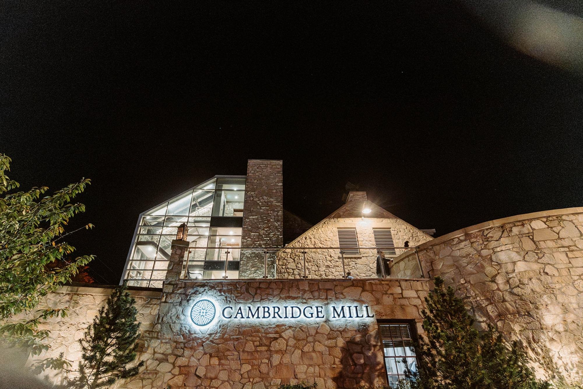 Nighttime exterior view of Cambridge Mill with illuminated signage and stone architecture.