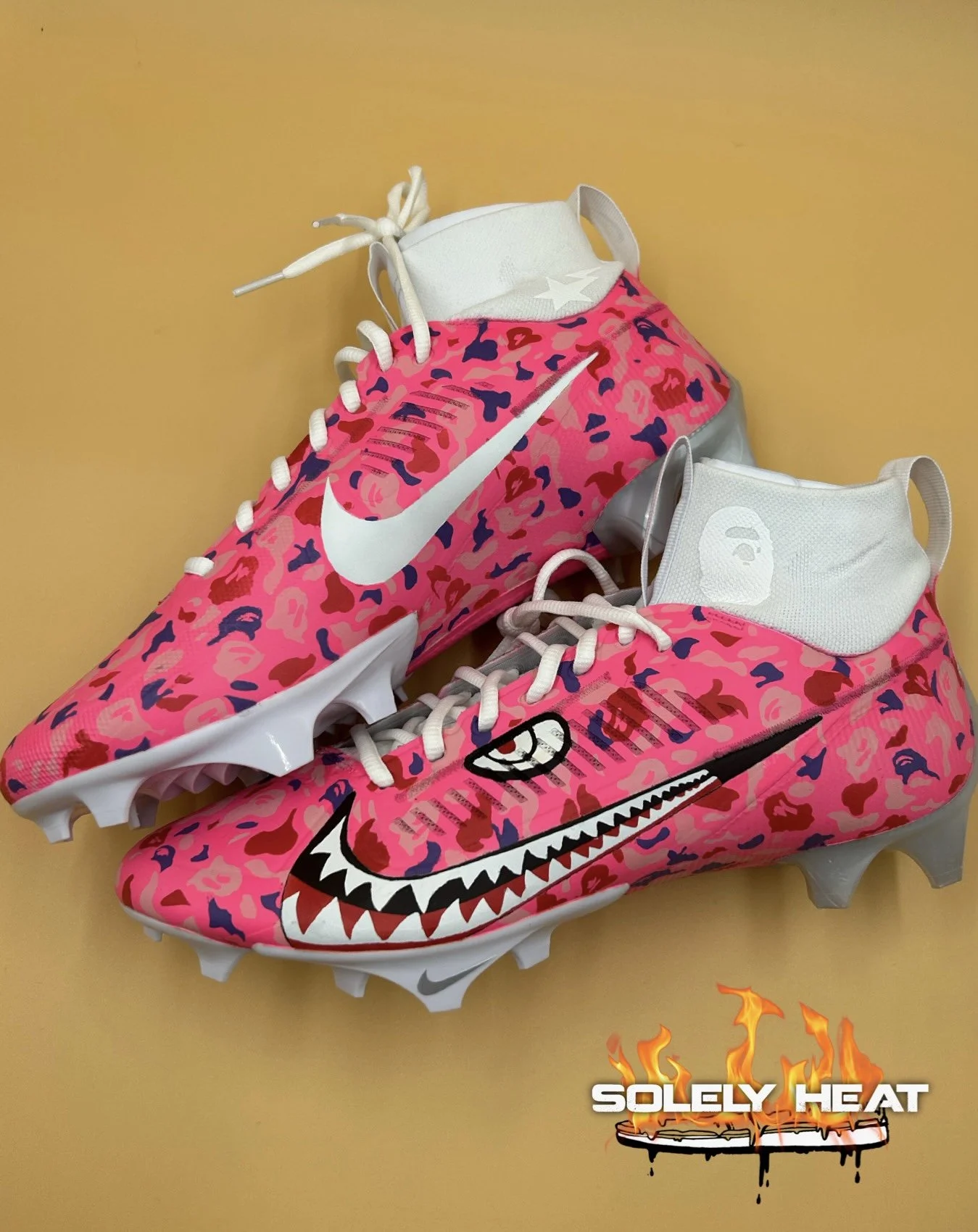 Hand-painted pink camouflage cleats with shark-mouth artwork by Solely Heat