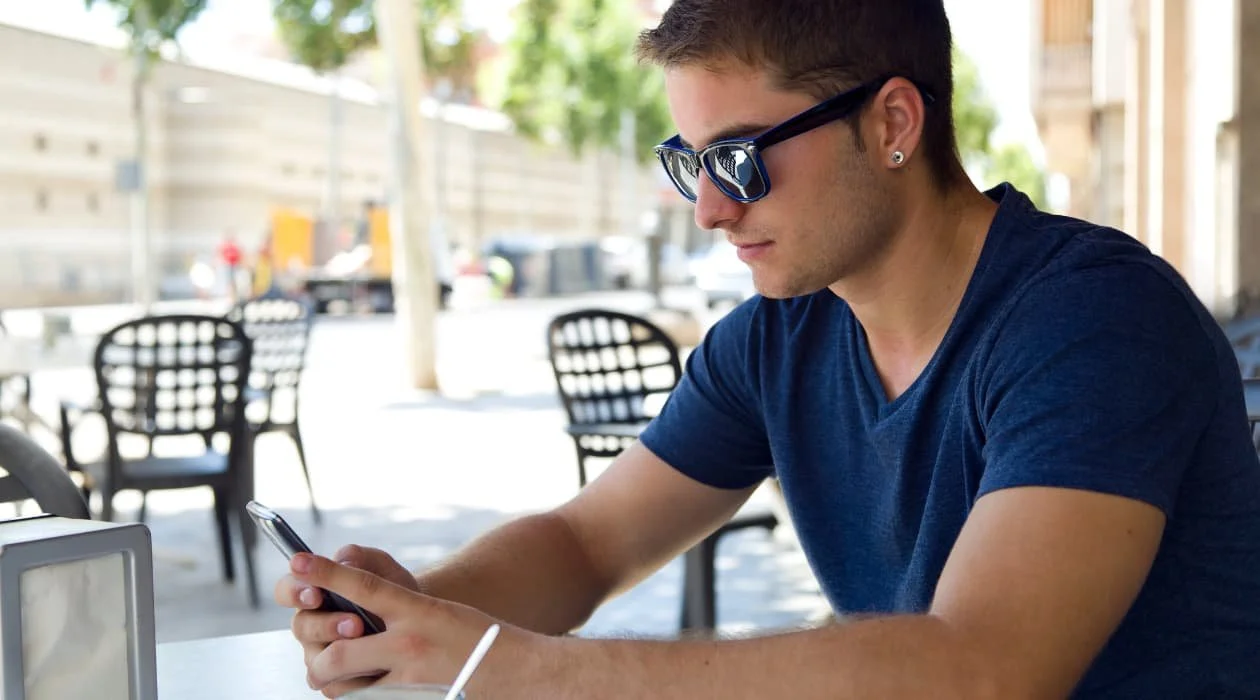 Guy swiping through his mobile phone while sitting outside.