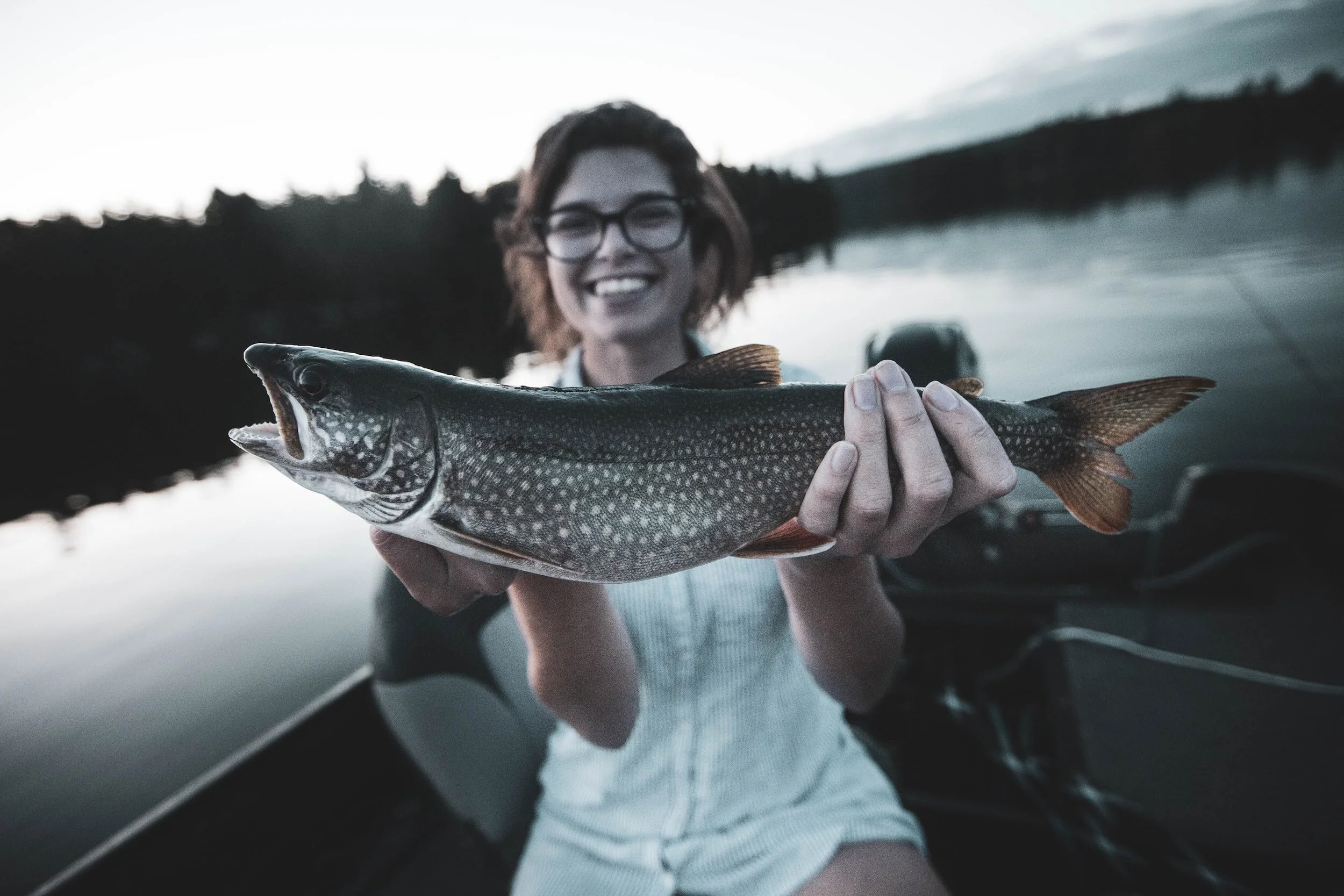 Person holding a fish on a boat with a lake in the background