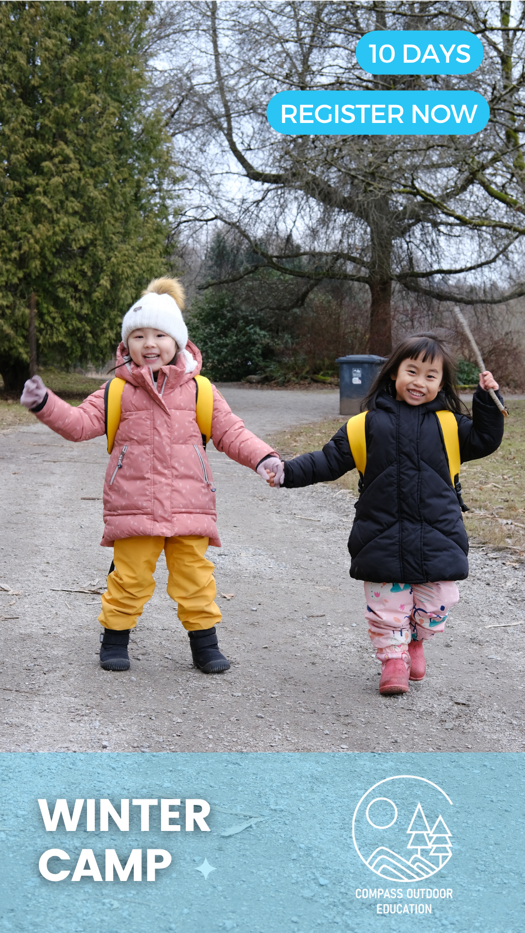 Two children in winter coats and backpacks holding hands and smiling on a forest path during Compass Outdoor Education winter camp in Vancouver.