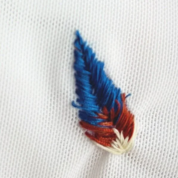 Blue, burnt orange, and cream embroidered feather on a white mesh cloth