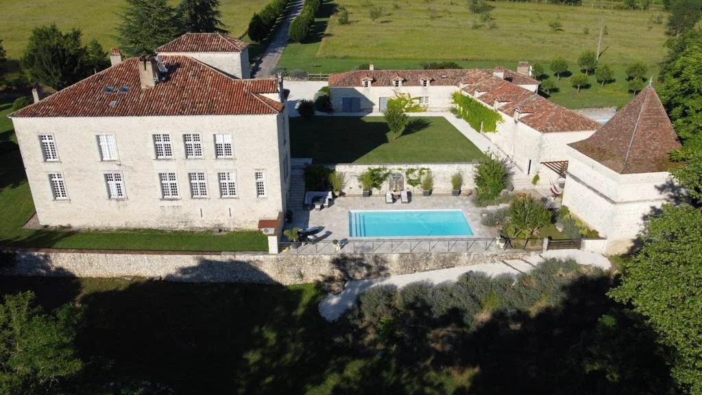 Vue aérienne d'une grande maison en pierre avec un toit en tuiles rouges, un espace de piscine, un jardin et des bâtiments autour.