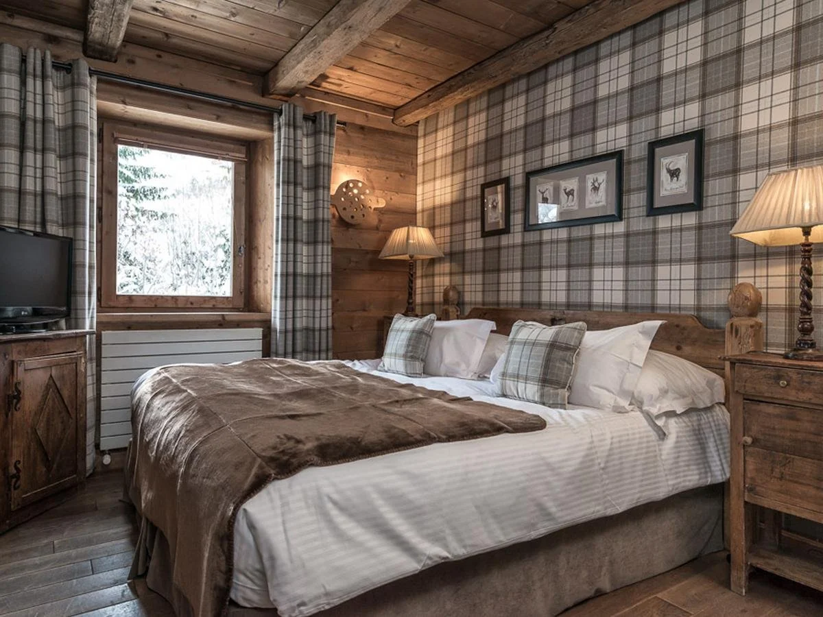 Chambre à coucher rustique avec un lit douillet et des décorations en bois, tableaux d'animaux sur le mur en tartan, lampes de chevet, fenêtre avec rideaux à carreaux.