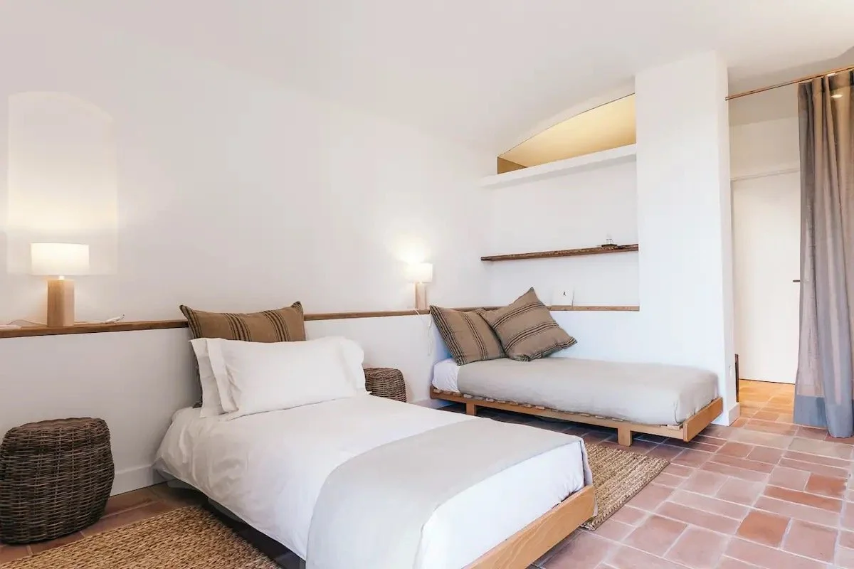 Chambre avec lit double, canapé-lit, deux lampes de chevet, tapis en jute, murs blancs, rideaux gris