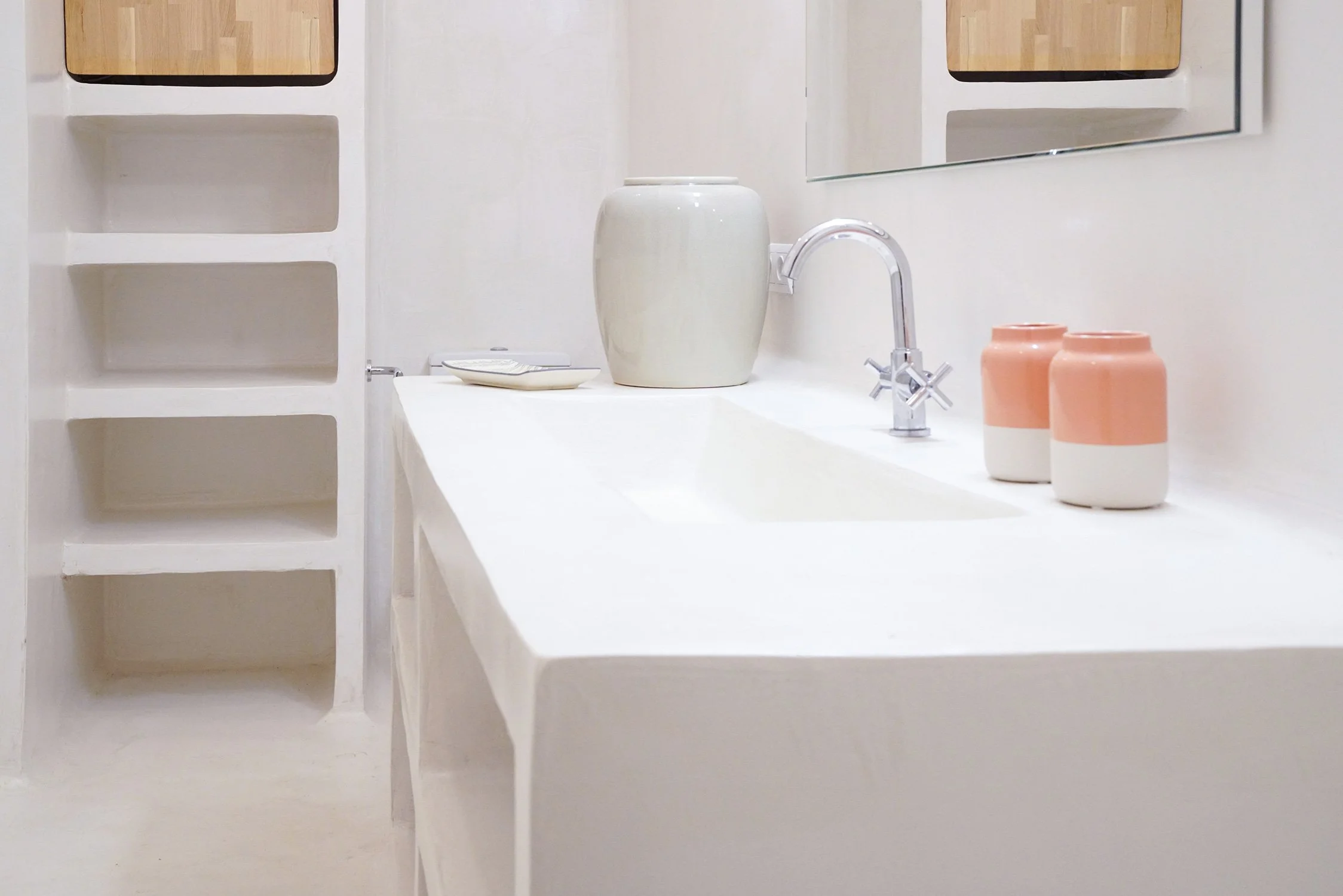 Intérieur d'une salle de bain blanche avec vasque, miroir, plantée et deux petits pots en céramique rose et blanc.