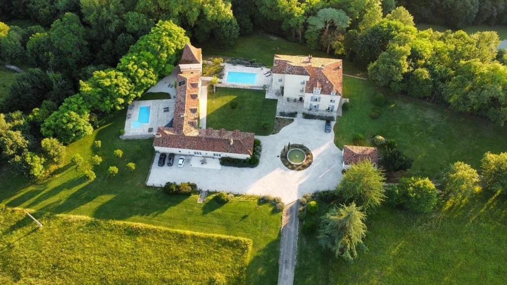 Vue aérienne d'une grande propriété résidentielle avec deux piscines, un parking, entourée d'arbres et de verdure.