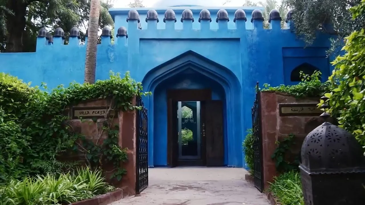 Une entrée bleue avec un cadre en arche accédant à une maison ou un bâtiment entouré de verdure.