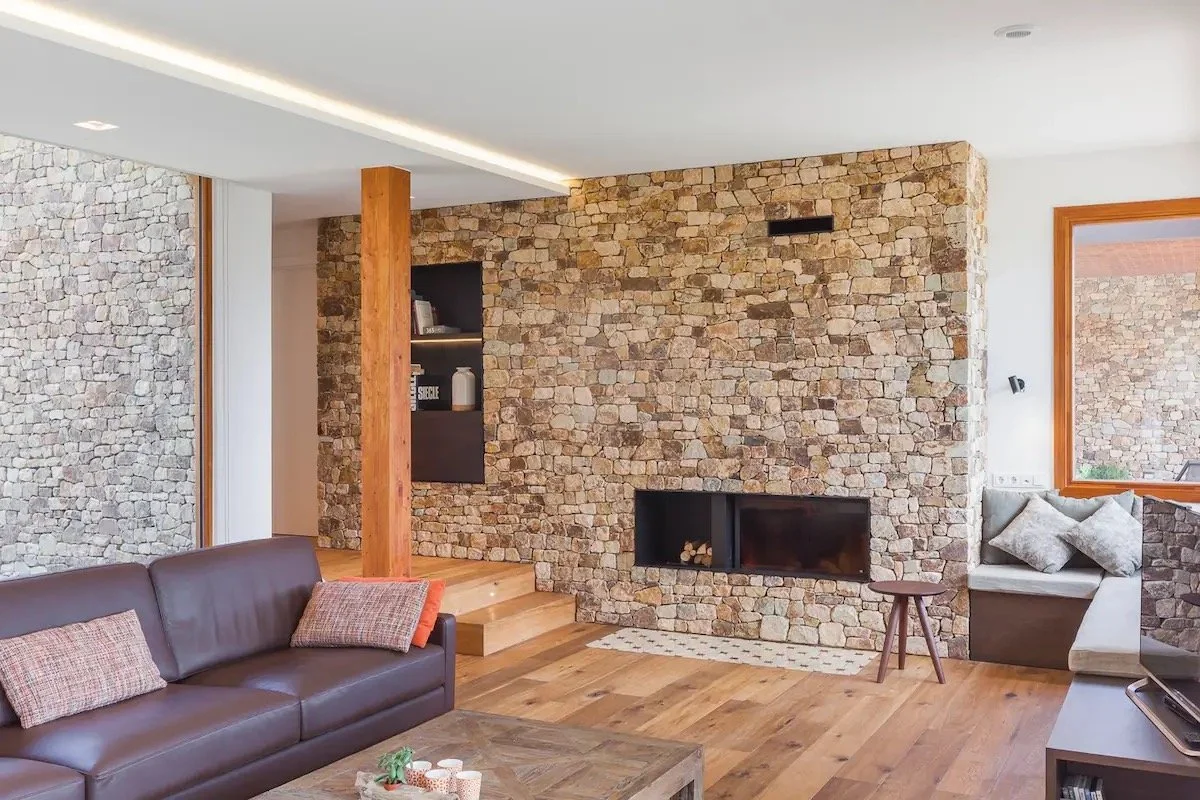 Salon contemporain avec cheminée en pierre, canapé en cuir marron, coussins en tissu à motifs, une petite table en bois, et un coin lecture près de la fenêtre avec coussins