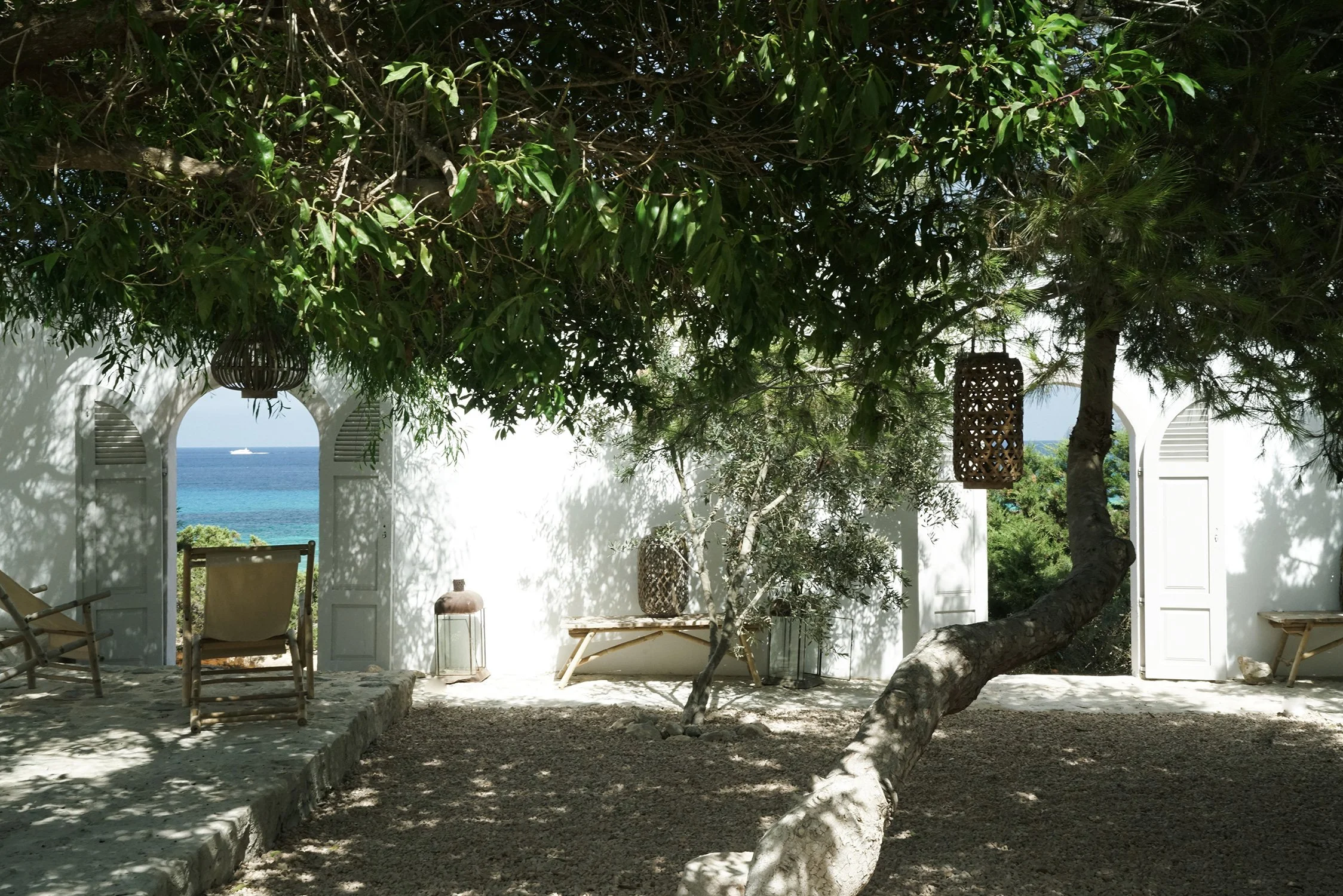 Terrasse ombragée avec branches d'un arbre, vue sur la mer à travers deux fenêtres ouvertes.