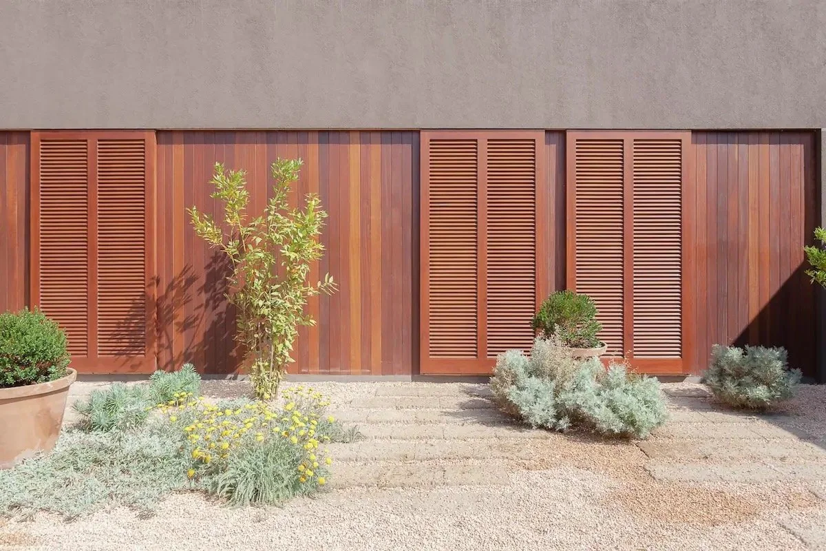 Mur en bois avec volets en bois, plantes en pot et autres végétation dans un jardin