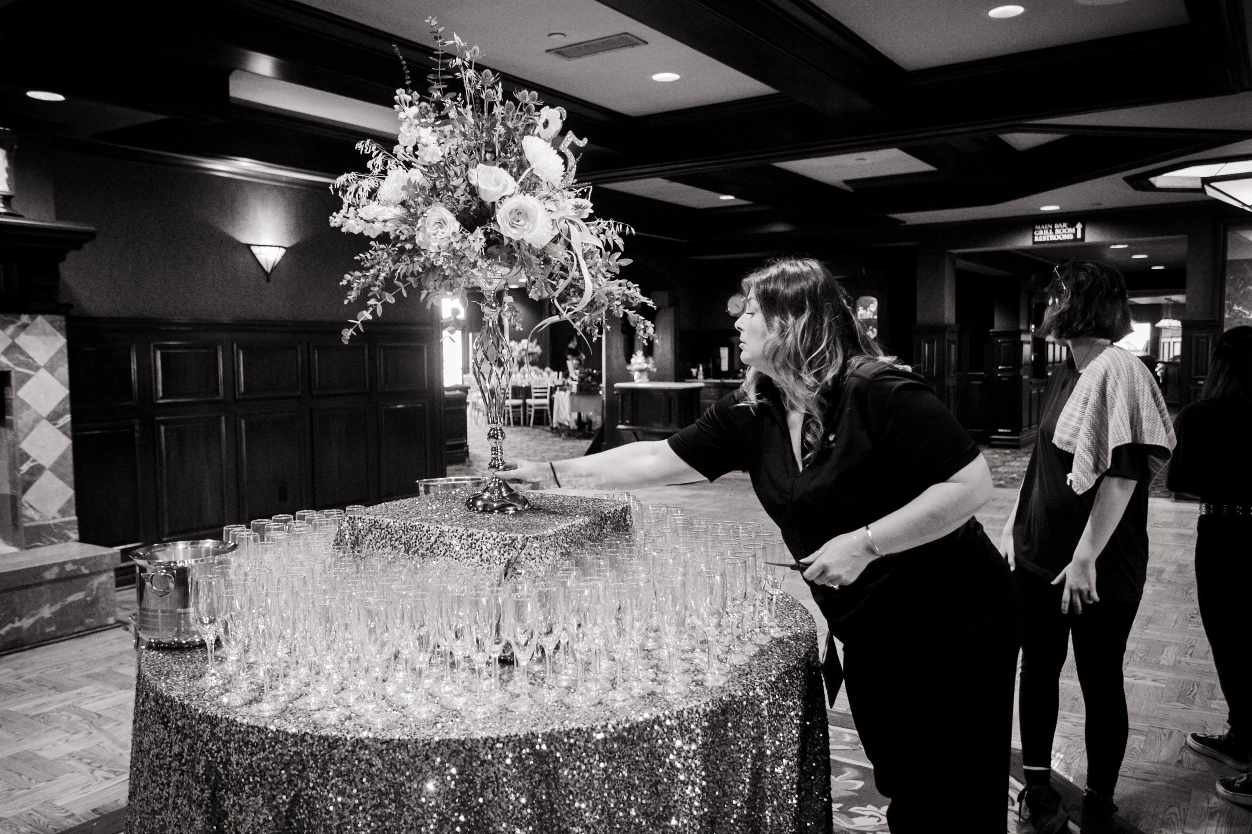 Floral Designer Rainy Diane adjusting Tall Floral vase Arrangement on top of Champagne toast table.