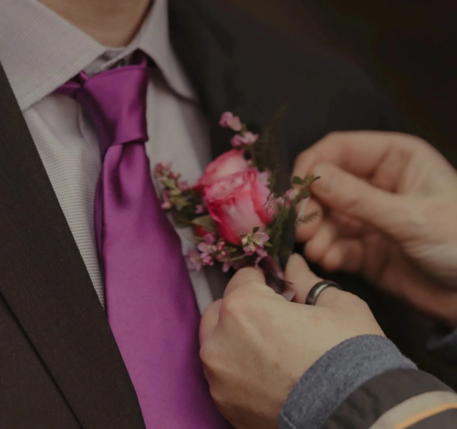 Rainy Diane's hands attaching grooms boutonniere. Pink spray rose, lavender filler. Joshua Tree.