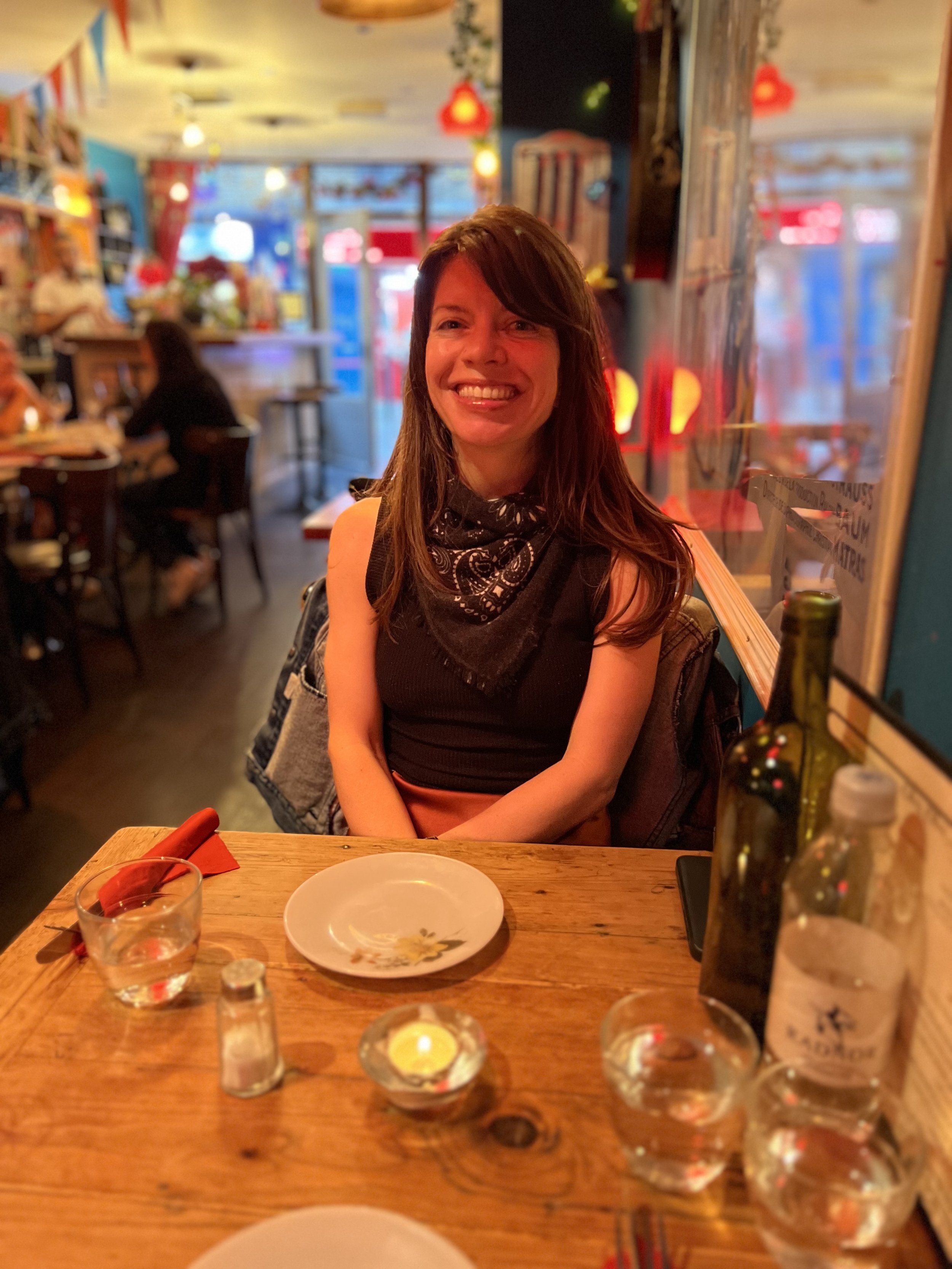 A woman with brown hair smiling at a restaurant table with empty plates and glasses.