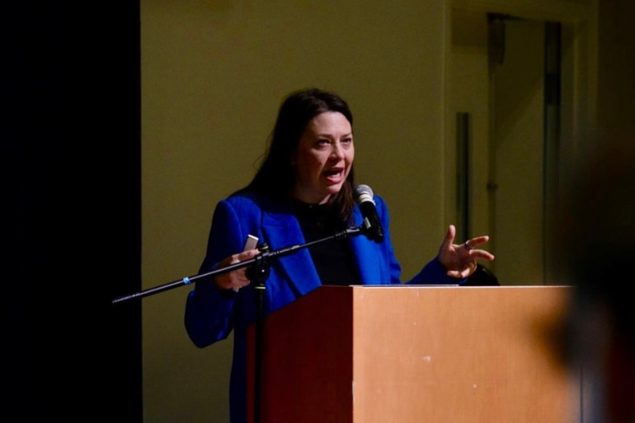 Nina Kaiser, Practice SF CEO, in a blue blazer speaking passionately at a wooden podium with a microphone.