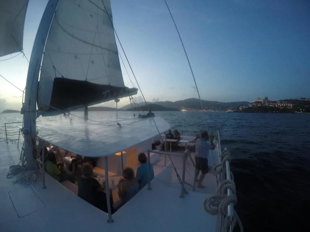 People on a boat sailing during dusk with a city skyline in the background.