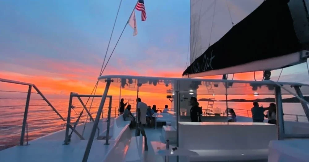 People on a boat during sunset with the sky painted in orange, pink, and purple hues.
