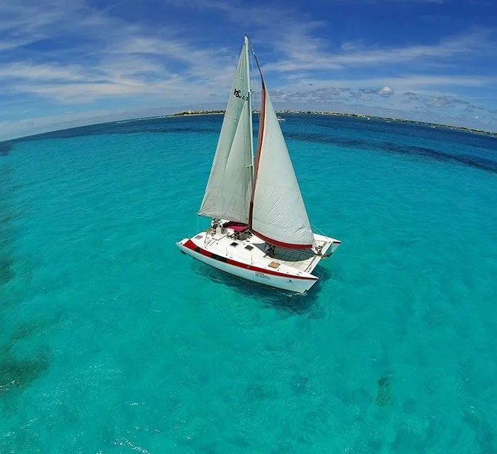 A sailboat with white sails floating on clear turquoise water under a partly cloudy sky.