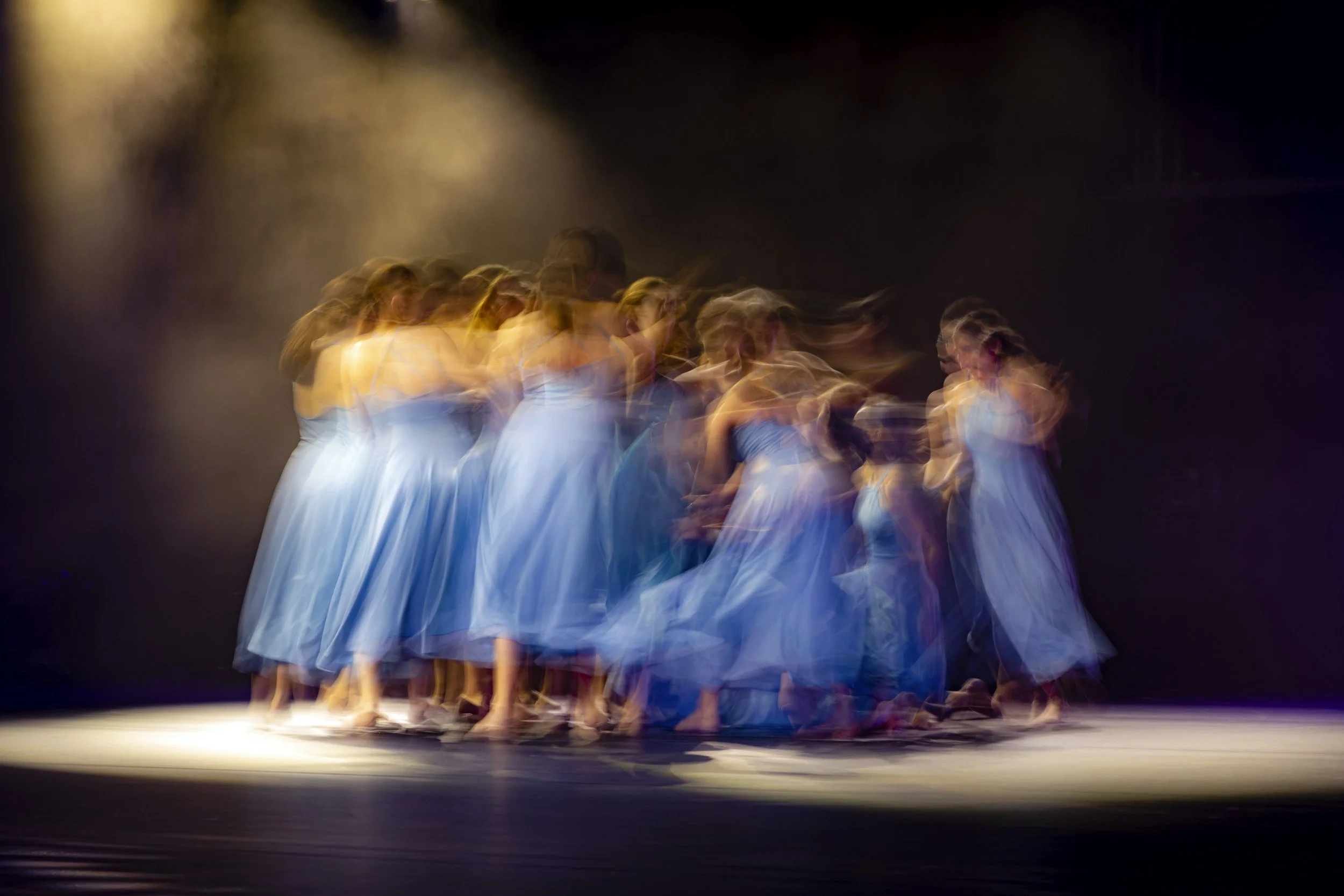 blurred image of a group of dancers on stage in blue dresses