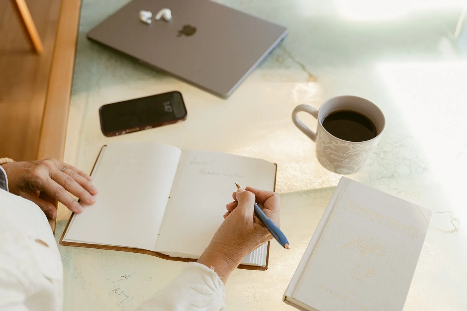 flat lay hand writing in journal with phone, laptop and coffee