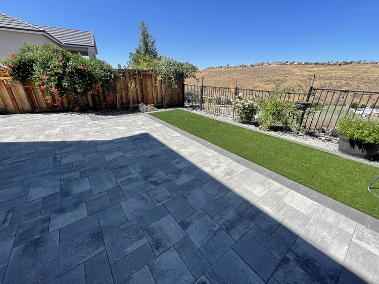 Large-format gray paver patio next to artificial turf and a wooden fence
