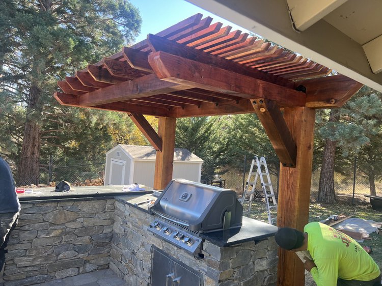 Built-in stainless steel grill in a stacked stone island under a wood pergola