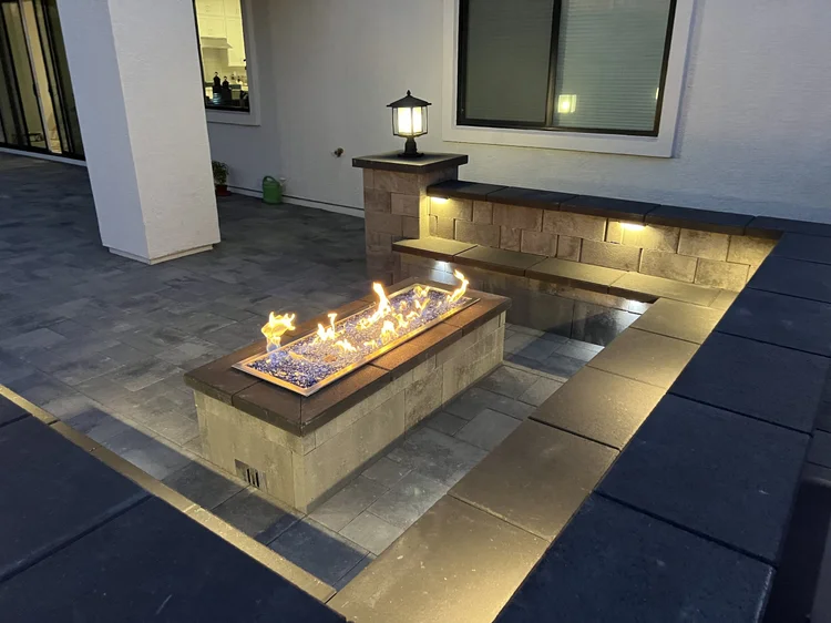Linear fire feature with a lamp pillar on a paver patio at night