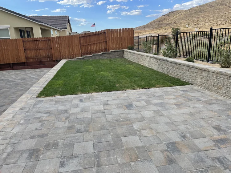 Block retaining wall around a lawn next to a gray paver patio
