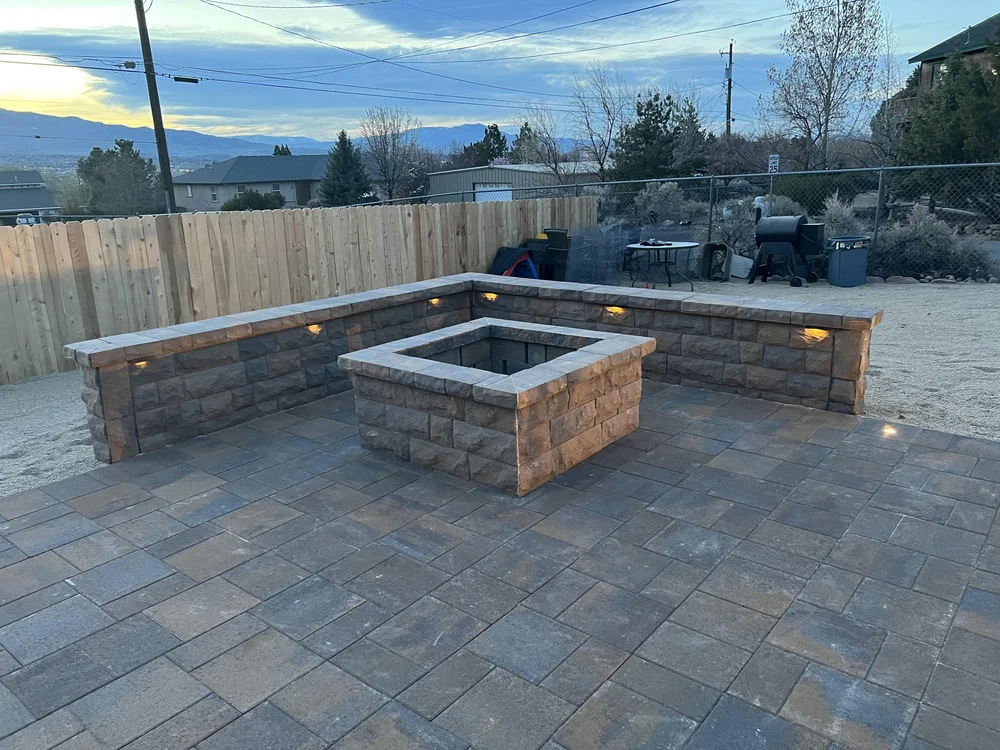 Square paver fire pit with a lit seating wall on a gray paver patio, built by Jefe's Design and Build