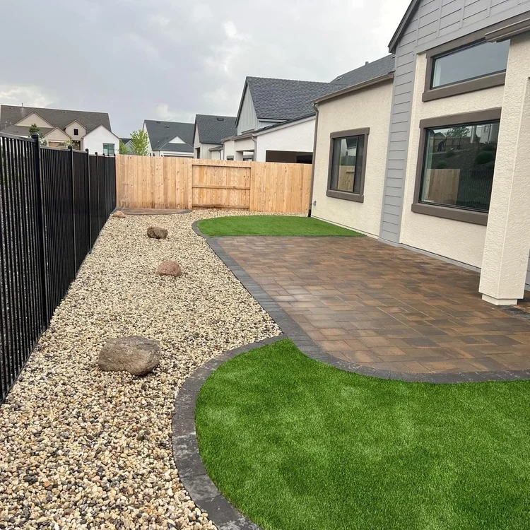 Side yard with river rock, boulders and artificial turf next to a paver patio