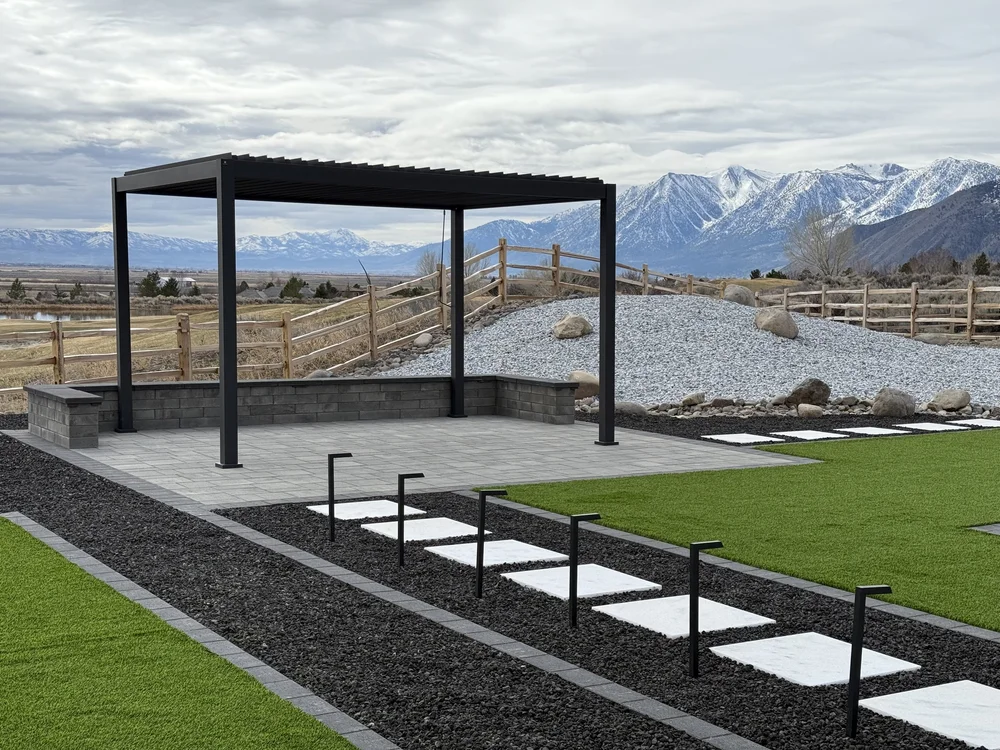 Modern black pergola over a paver patio with a seating wall and gravel beds, with snow-capped mountains in the background, built by Jefe's Design and Build