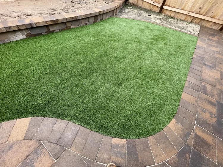 Curved artificial turf area bordered by brick pavers